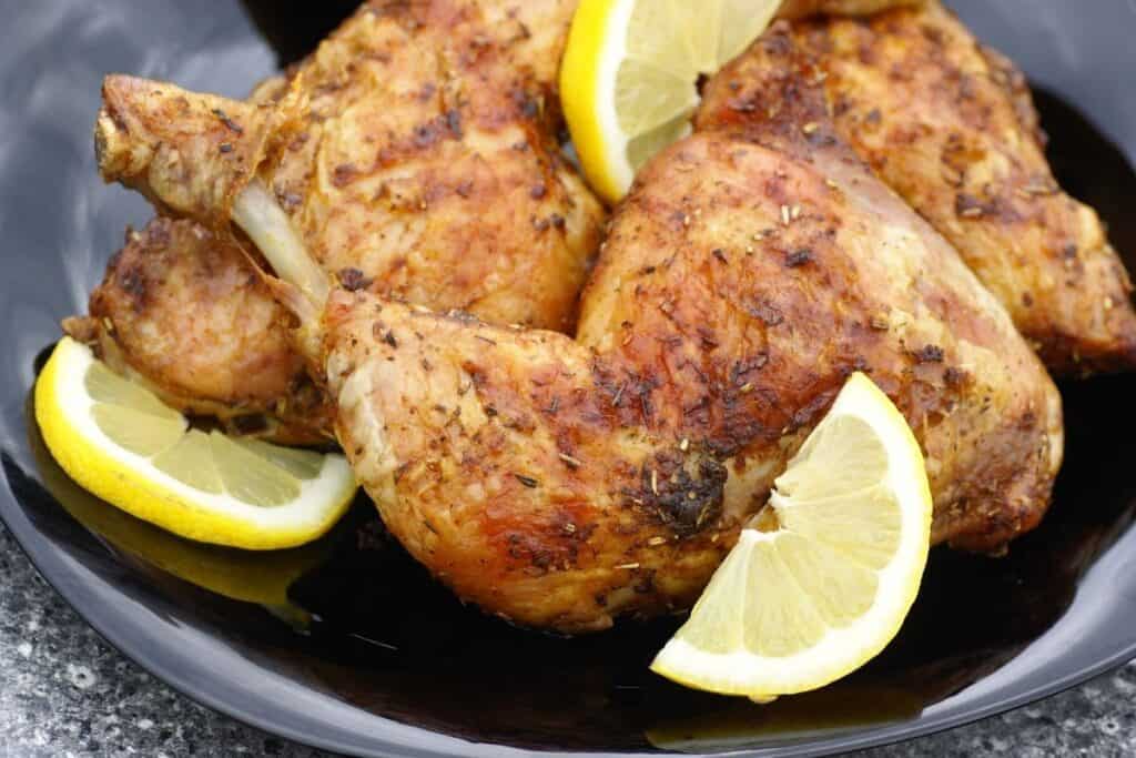 Roasted chicken legs and thighs with fresh lemon wedges on a platter.