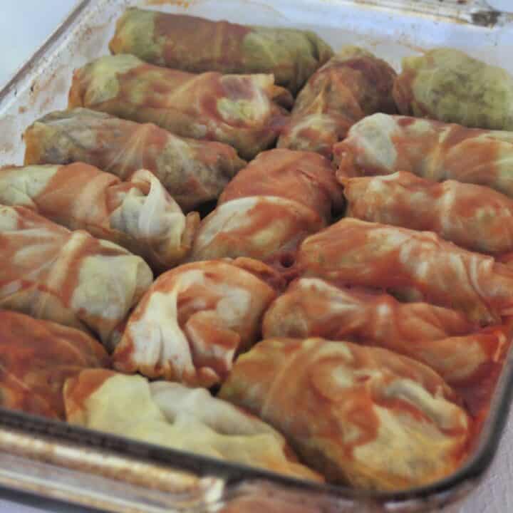 A glass baking tray full of cooked cabbage rolls covered in tomato juice.