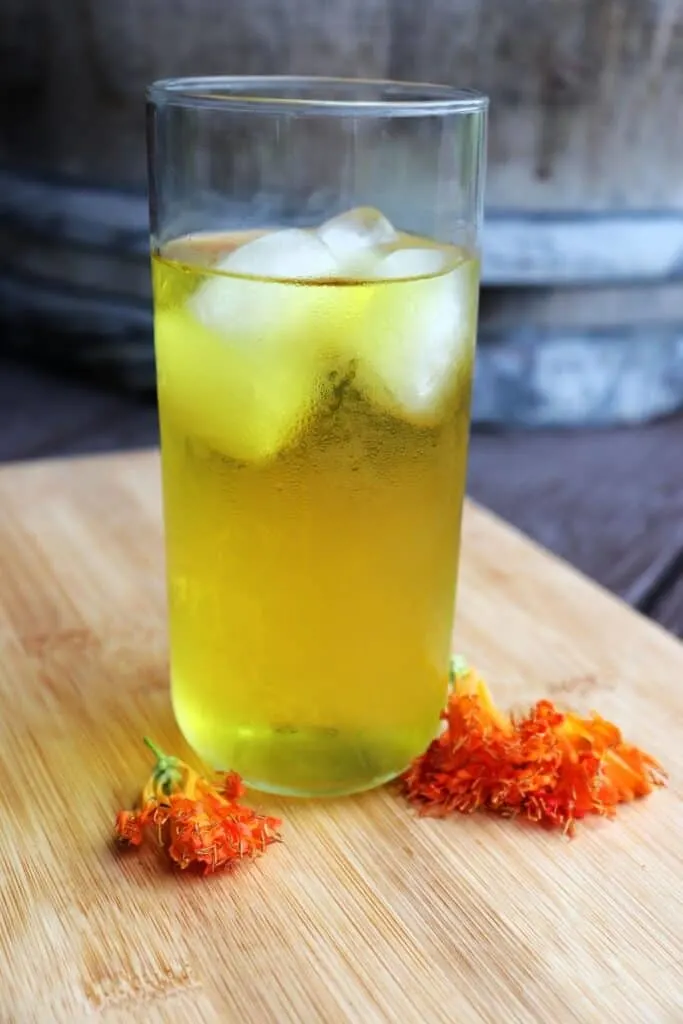 A glass of iced honeysuckle tea on a wooden board surrounded by orange honeysuckle flowers.
