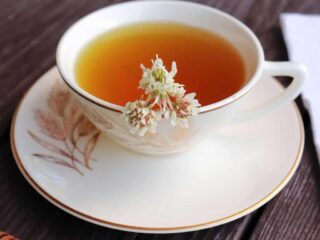 A teacup filled with tea sitting on a saucer, white clover flowers floating in the tea.