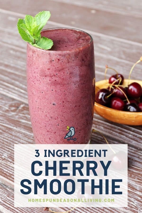 A glass full of cherry smoothie with a mint sprig on top and a wooden bowl of fresh cherries in the background. A text overlay reads: 3 ingredient cherry smoothie.