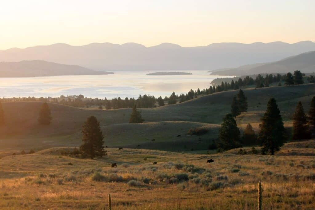 Rolling hills looking toward a large lake with hazy sky and mountains in the background.