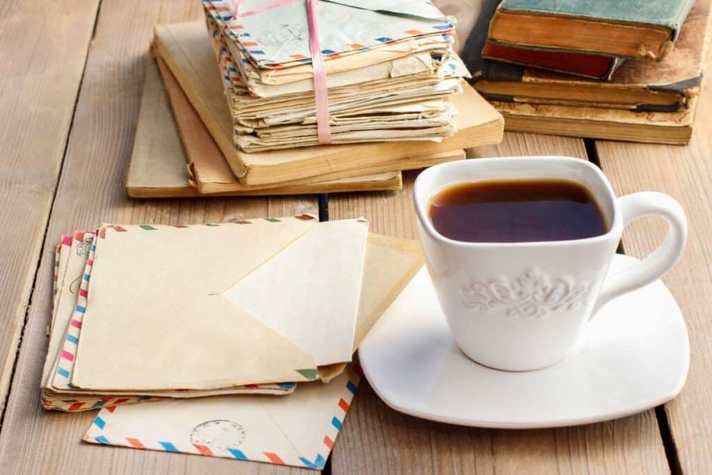 Stacks of letters and old books on table with a cup of coffee.