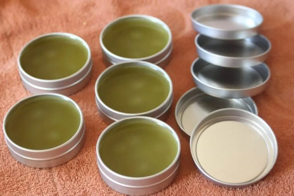5 tins full of green salve sitting on a towel with lids sitting next to them.