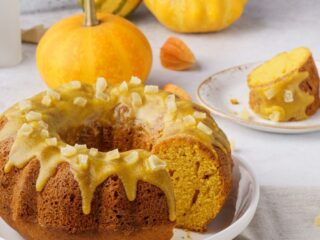 A glazed bundt cake on a plate with a single slice in the background and fresh winter squash.