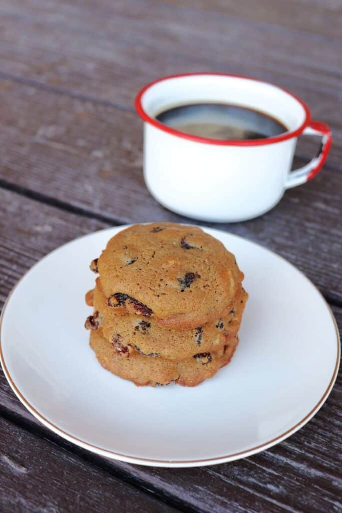 3 hermit cookies stacked on a plate with a cup of coffee in the background.