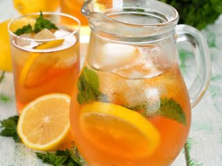 A pitcher of iced tea surrounded by glasses and orange slices.