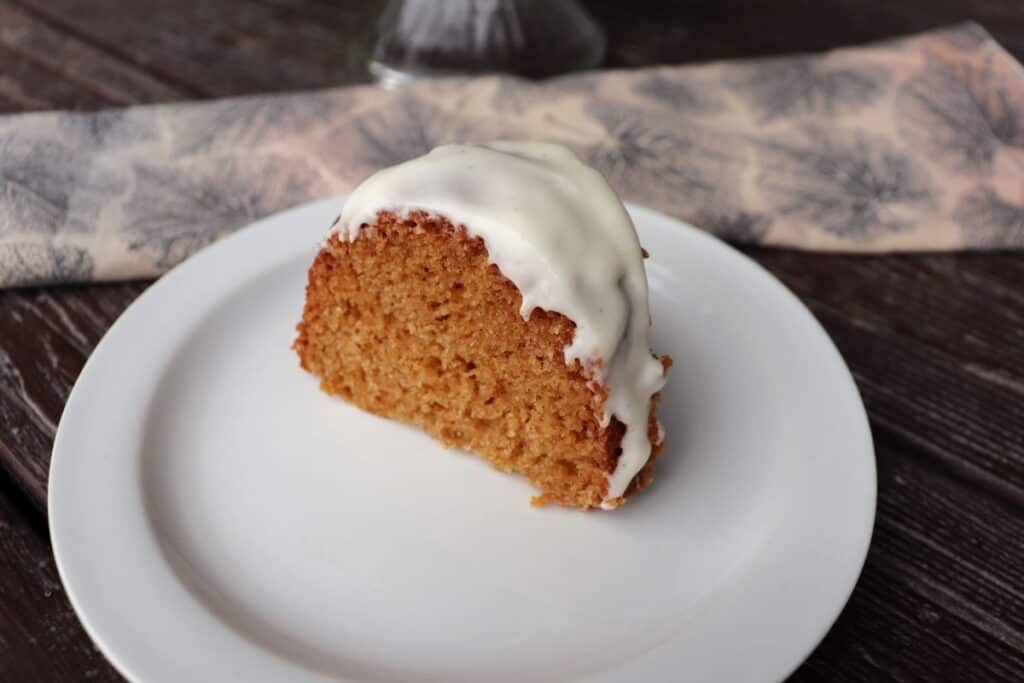 A slice of applesauce bundt cake on a plate with a napkin in the background.