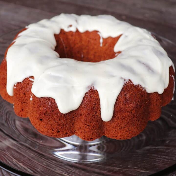 An applesauce bundt cake with vanilla glaze sitting on a glass cake plate.