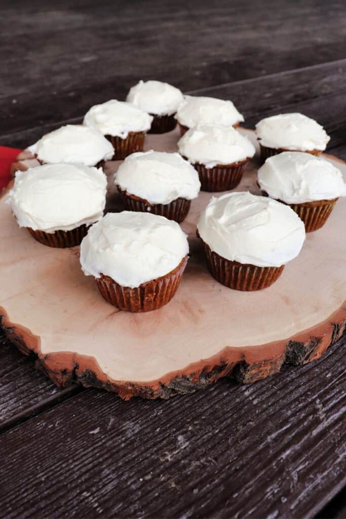Applesauce cupcakes with a white frosting arranged on a wooden plank platter.