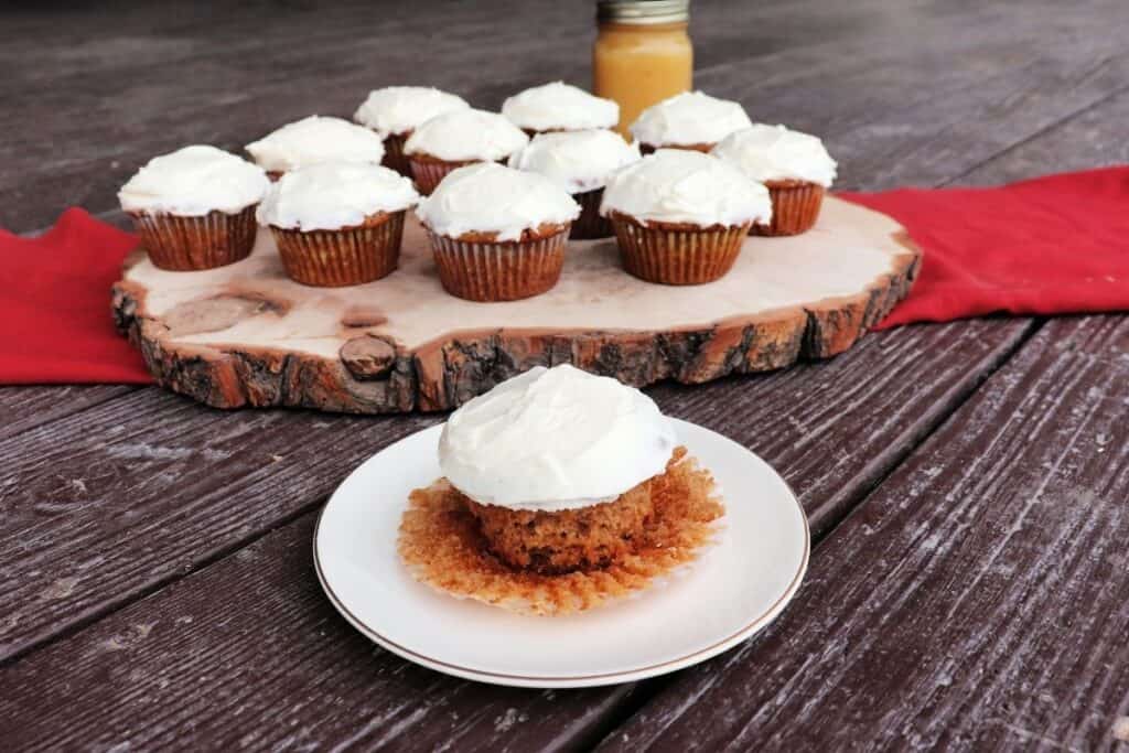 An applesauce cupcake on a plate with a platter of more cupcakes and a jar of applesauce in the background.