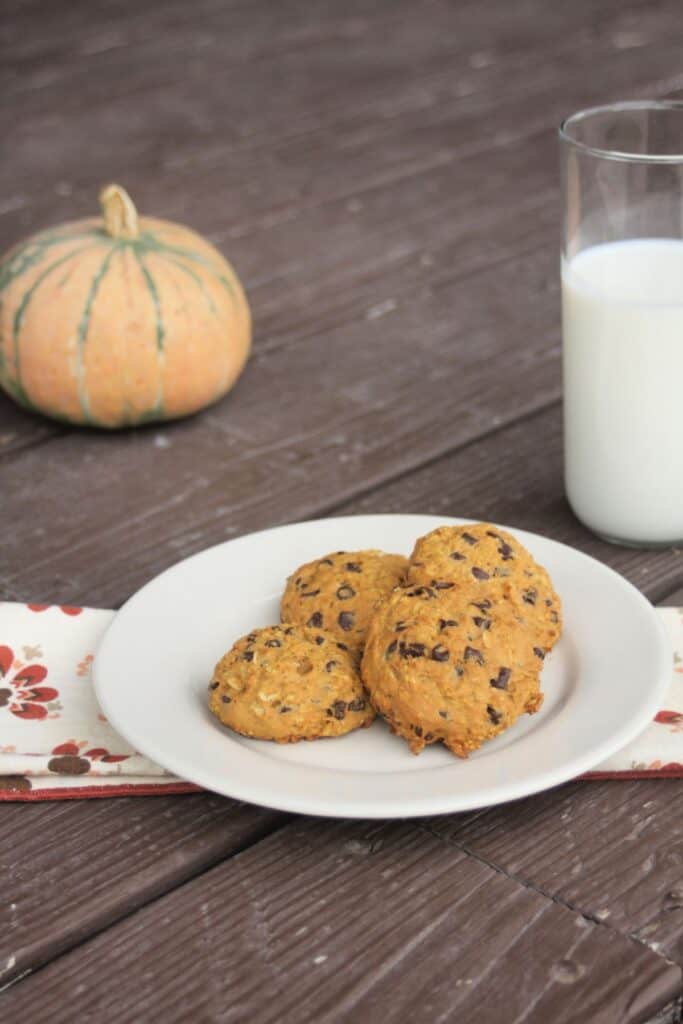 Pumpkin oatmeal cookies on a plate with a glass of milk and a pumpkin in the background.