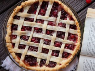 A lattice topped cherry pie as seen from above with an open cookbook sitting next to it.