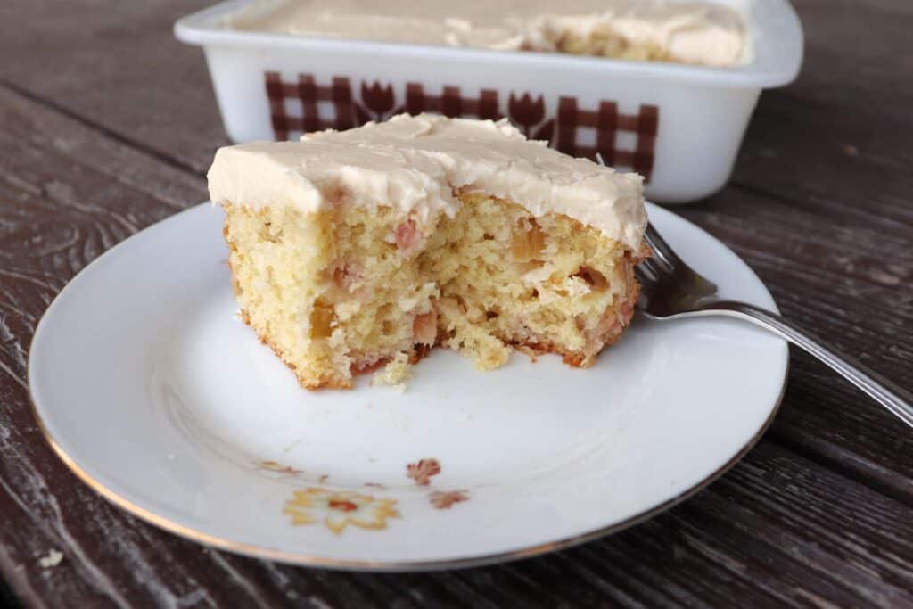 A piece of cake on a plate with a bite taken out of it, a fork sits with it. Remaining cake still in pan behind it.