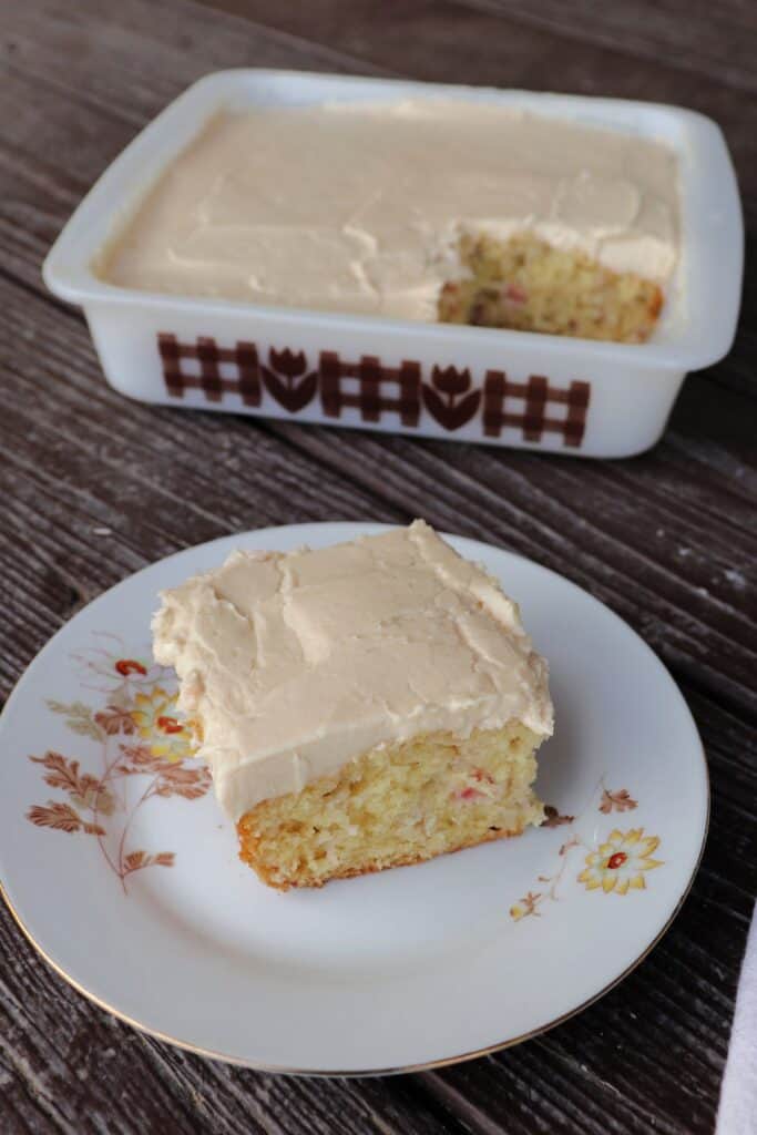 A piece of rhubarb cake on a plate with remaining cake in pan behind it.