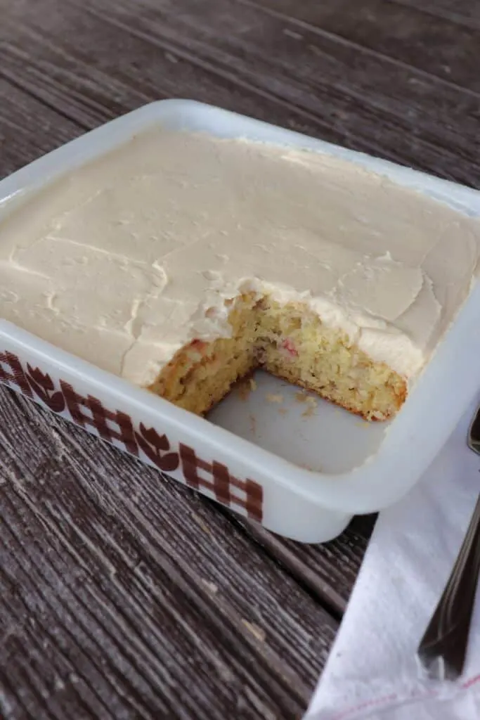 Rhubarb cake with caramel frosting in a square pan with one piece removed.