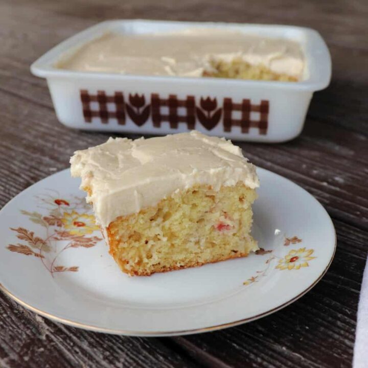 A piece of rhubarb cake on a plate with remaining cake in pan behind it.