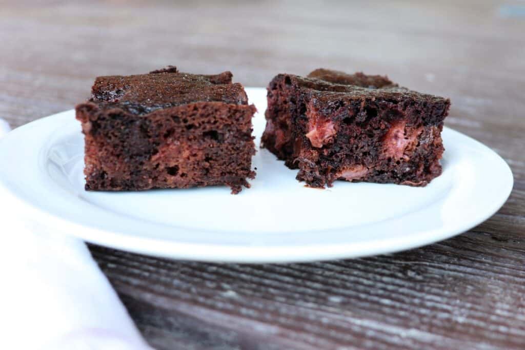 Two brownies on a plate exposing red bits of strawberries inside, a white napkin sits to the left of the plate.