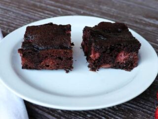 Two brownies on a plate exposing red bits of strawberries inside.