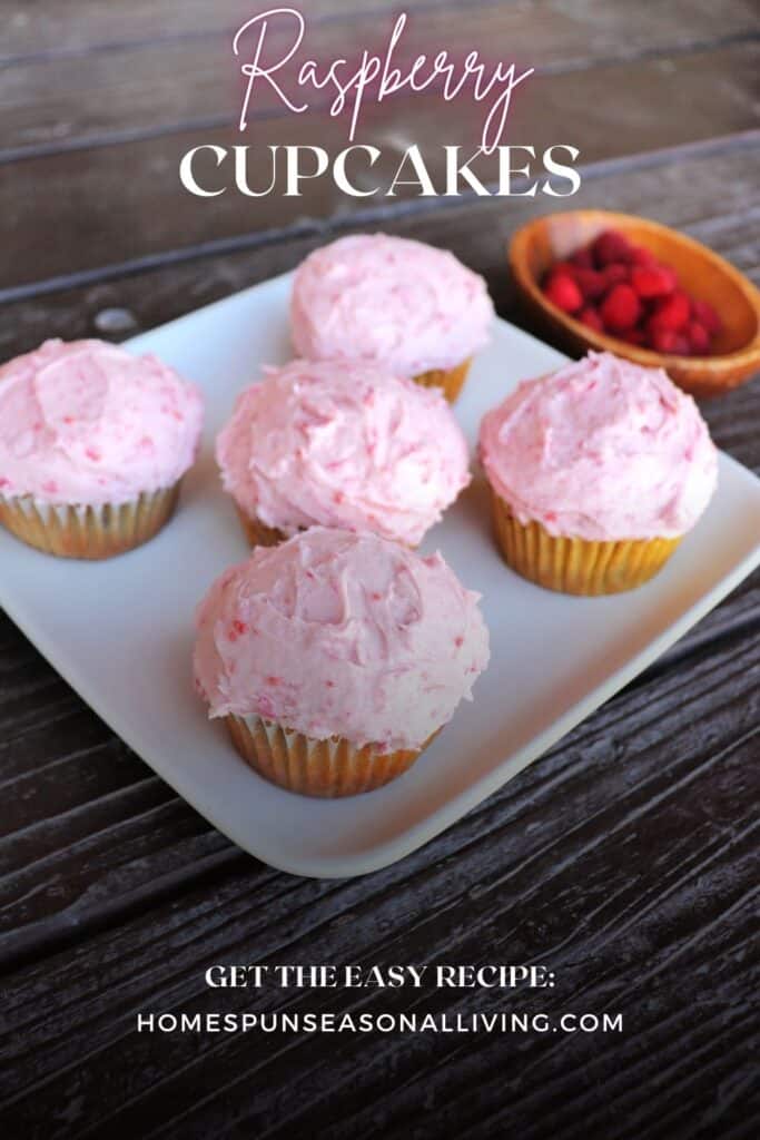 5 cupcakes with pink frosting sit on a platter. A wooden bowl with fresh raspberries sits in the background. Text overlay reads: Raspberry Cupcakes.