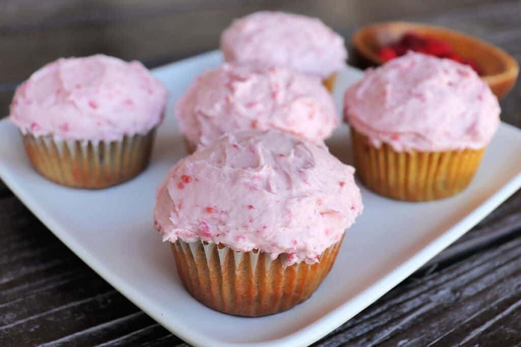 Raspberry cupcakes sit on a platter, as seen from the side with paper liners exposed.
