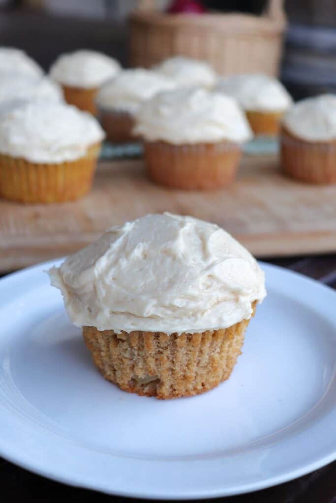 Close-up of a frosted cupcake sitting on a white plate, more cupcakes in the background.