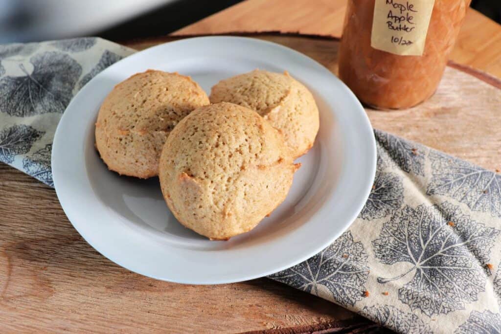 Close up of apple butter cookies on a plate that is sitting on a leaf patterned napkin. A jar of apple butter sits behind it.