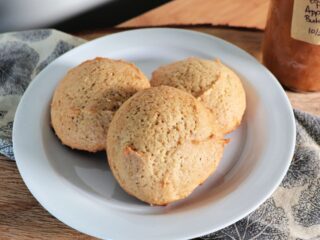 Cookies on a white plate that is sitting on a napkin, a jar of apple butter sits in the background.