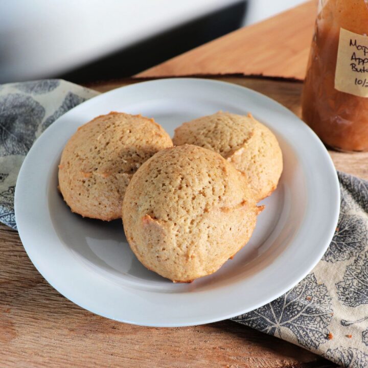 Cookies on a white plate that is sitting on a napkin, a jar of apple butter sits in the background.