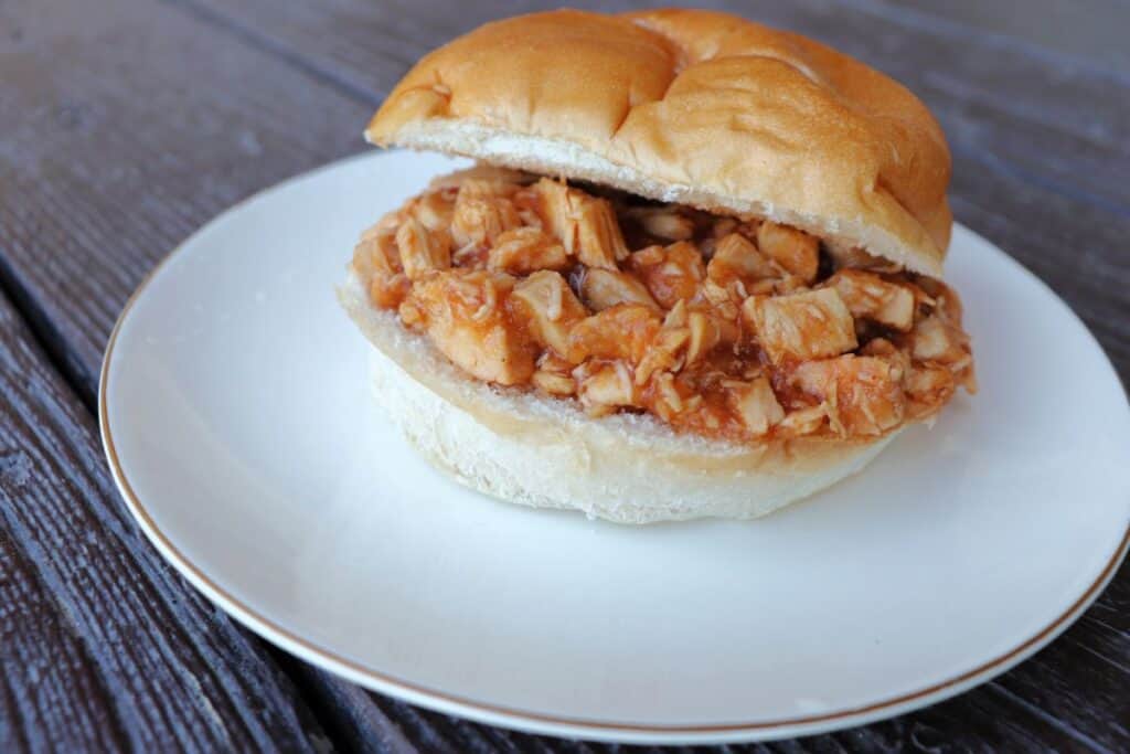 A split bun sitting on a plate with applesauce bbq chicken sitting in between the slices.