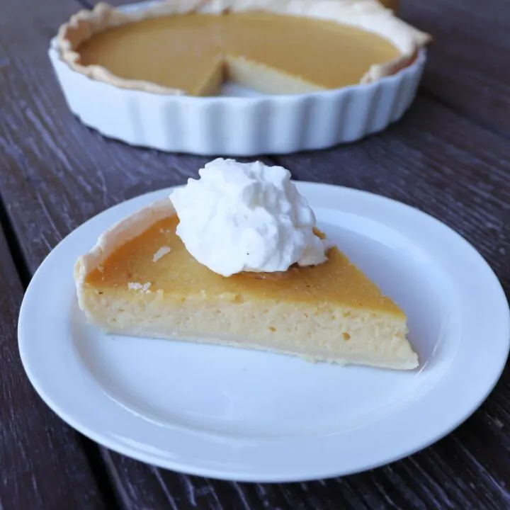 A slice of applesauce pie topped with whipped cream, remaining pie sits in the background.