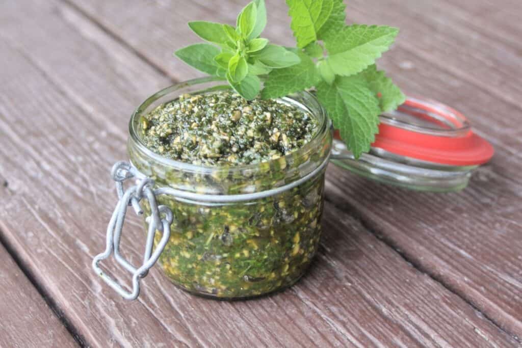 An open glass jar full of pesto with fresh herb leaves sitting on top.