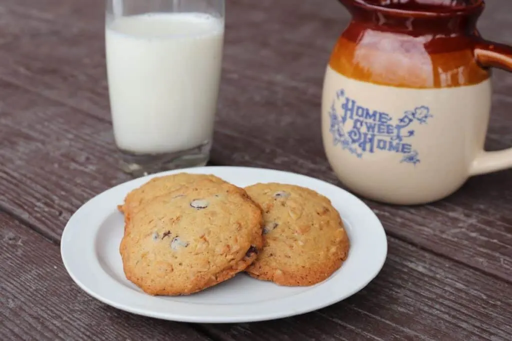 Granola cookies on a plate. A glass of milk and an earthen pitcher with the words 'home sweet home' on it sit in the background. 