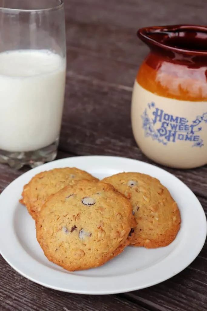 Granola cookies on a plate. A glass of milk and an earthen pitcher with the words 'home sweet home' on it sit in the background. 