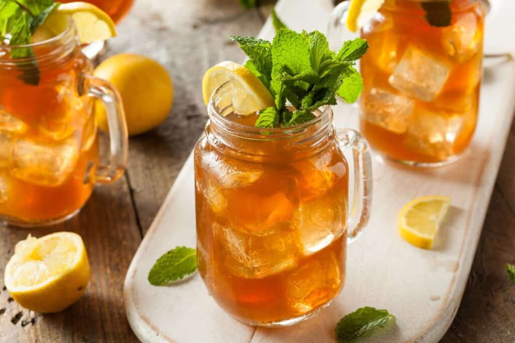 Glasses of iced tea garnished with sprigs of fresh mint and lemon slices sit on a table.