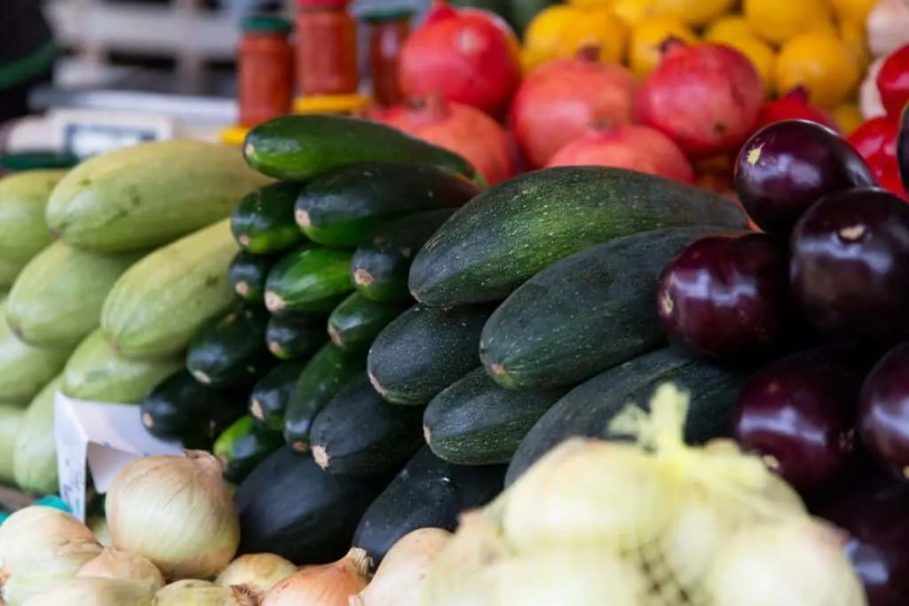 A variety of summer squash and other summer vegetables on a shelf at the farmers market.