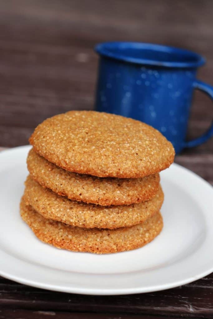 A stack of spice drop cookies sit at an angle on a white plate on a table with a blue tin cup in the background.