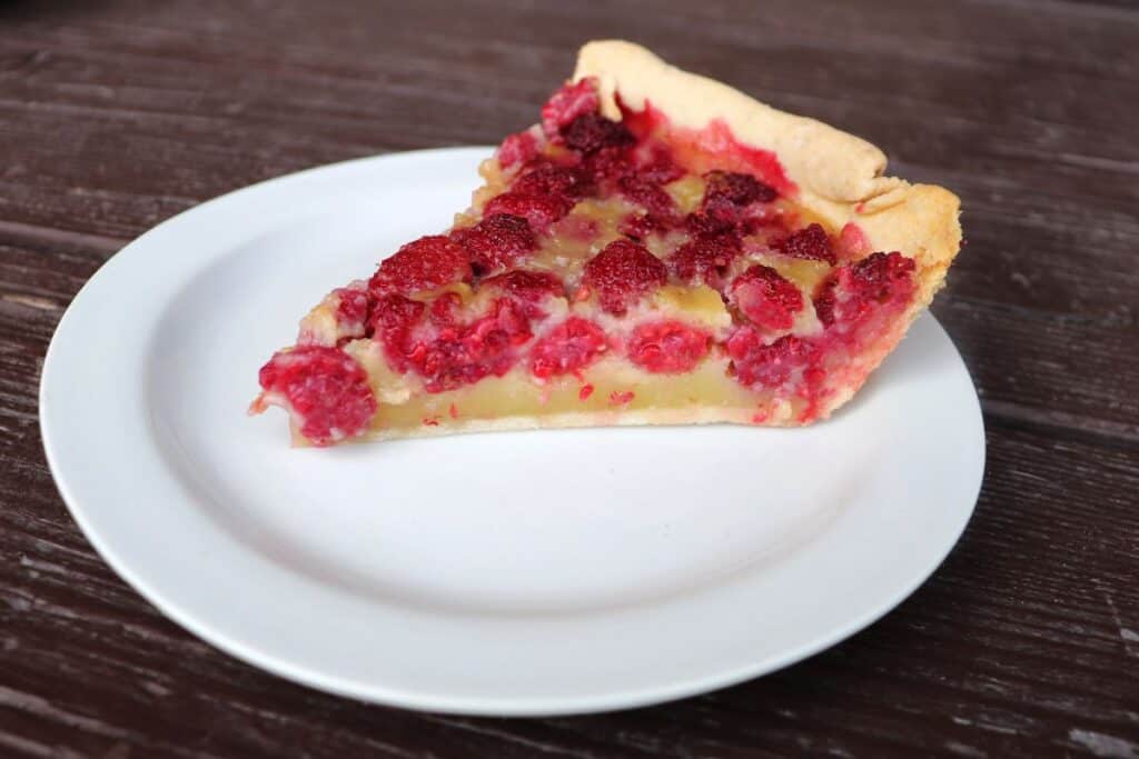 A slice of raspberry custard pie as seen from the side sits on a white plate. 