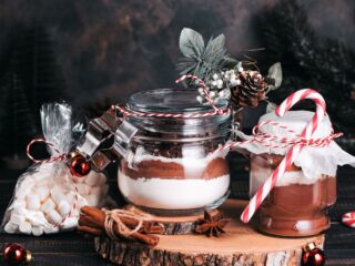 Jars of layered mixes sit on a wooden board surrounded by whole spices and decorated with ribbons.