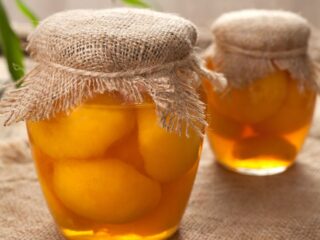 2 jars of peaches in glass jars with burlap covering the lids sit on a table.