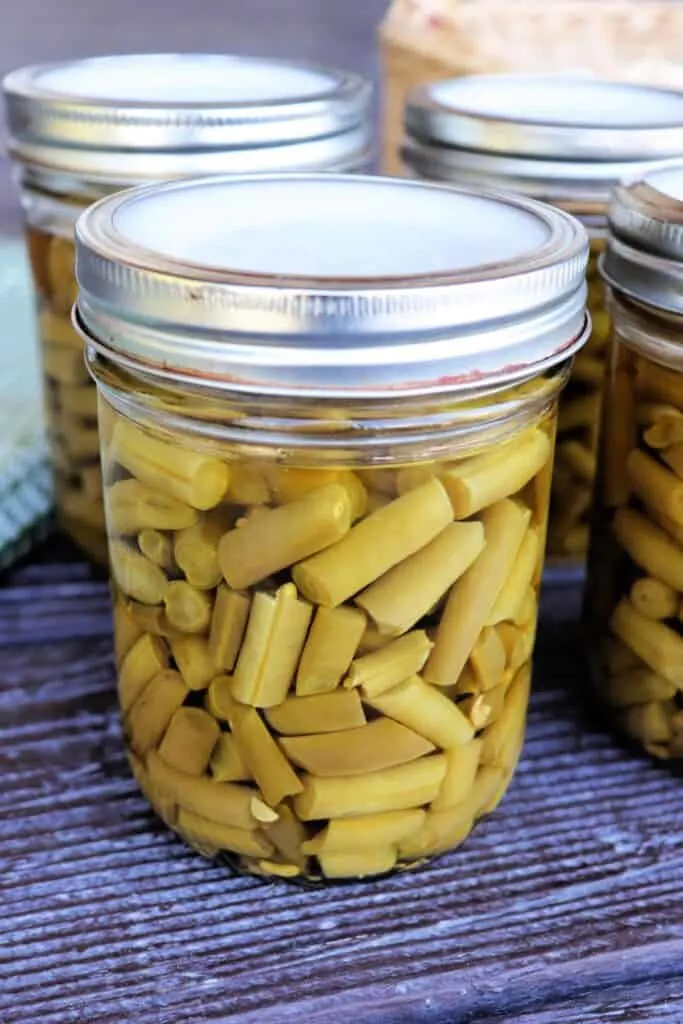 Close up of a glass jar full of green beans with more jars in the background. 