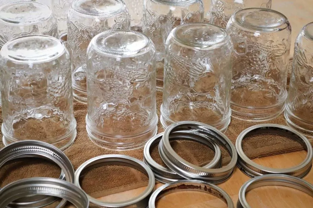 Empty canning jars sitting upside down on a towel with canning rings sitting in front. 