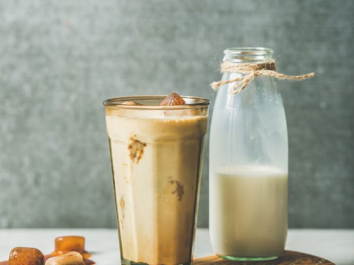 A glass of iced coffee sits on a table with a bottle of milk behind it.