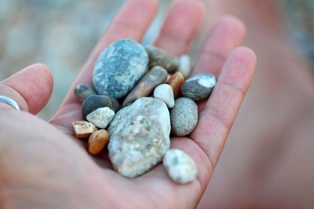 A white woman's hand holding a collection fo pebbles and stones. 