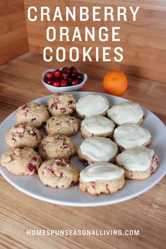 Cranberry orange cookies sit on a plate, some have frosting, some do not. Behind the plate is a bowl of fresh cranberries and and an orange. Text overlay reads: Frosted Orange Cookies.