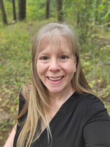 A picture of Kathie Lapcevic standing in the forest.