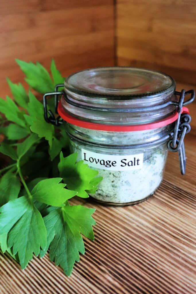 A closed jar labeled 'lovage salt' sits on a table next to fresh lovage leaves.