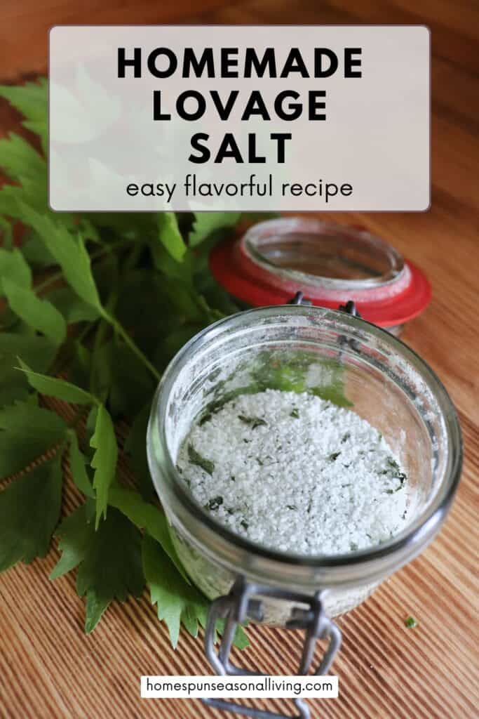 An open glass jar sits on table, inside the jar is salt and dried herbs all mixed together. next to the jar is a stalk of fresh lovage leaves. Text overlay reads: Homemade Lovage Salt - easy flavorful recipe.