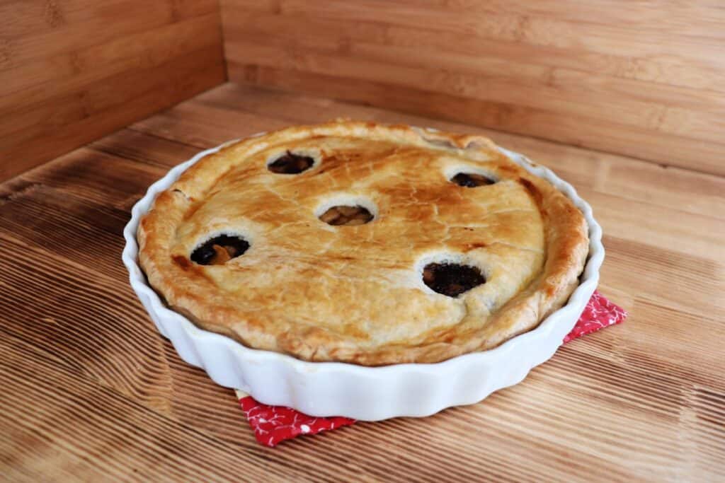 A whole pie sits on a table. The pie has a golden crust with holes cut out for venting on top. 